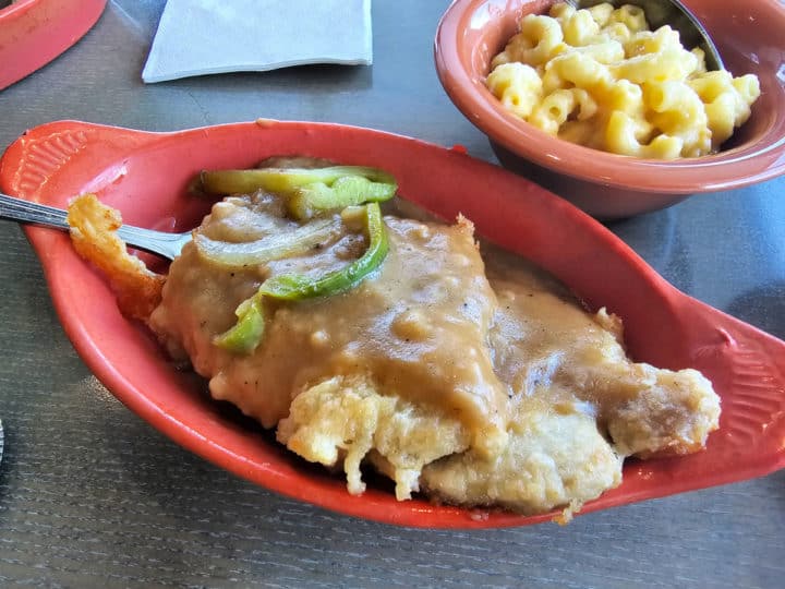 Chicken fried pork chops covered in gravy in a red bowl next to a bowl of mac n cheese