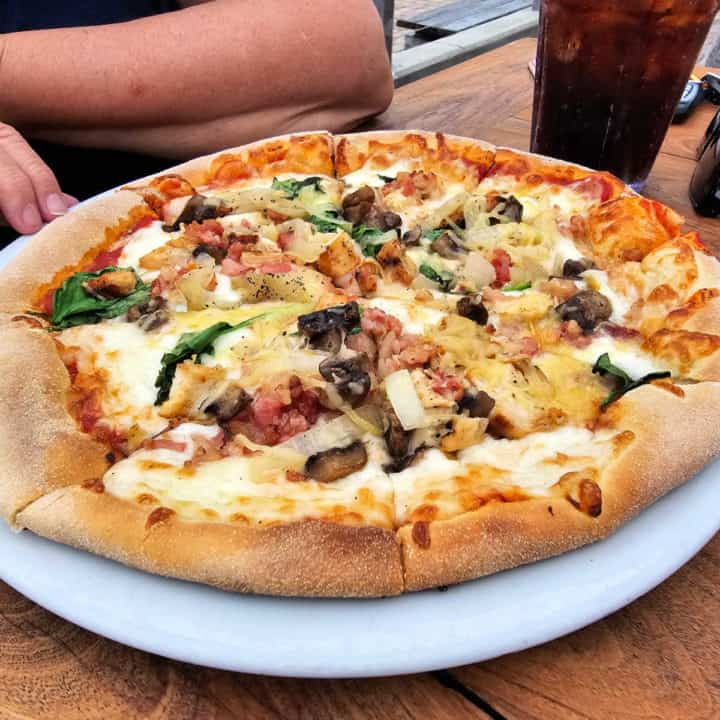 Pizza with grilled chicken, bacon, spinach, mushrooms and onions on a white plate