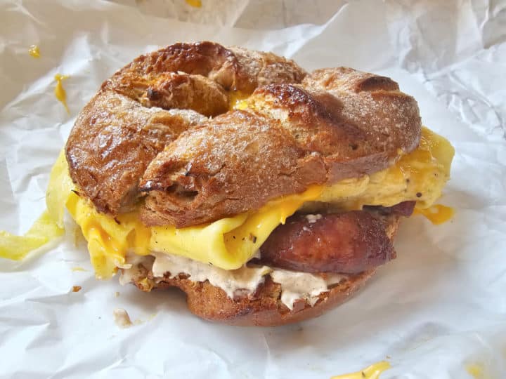 French toast bagel with eggs, sausage, and schmear on a white paper Bagel Boy