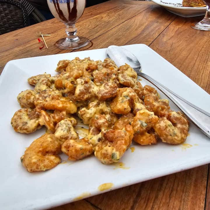Firecracker shrimp on a white plate with a large spoon next to a Bushwacker cocktail