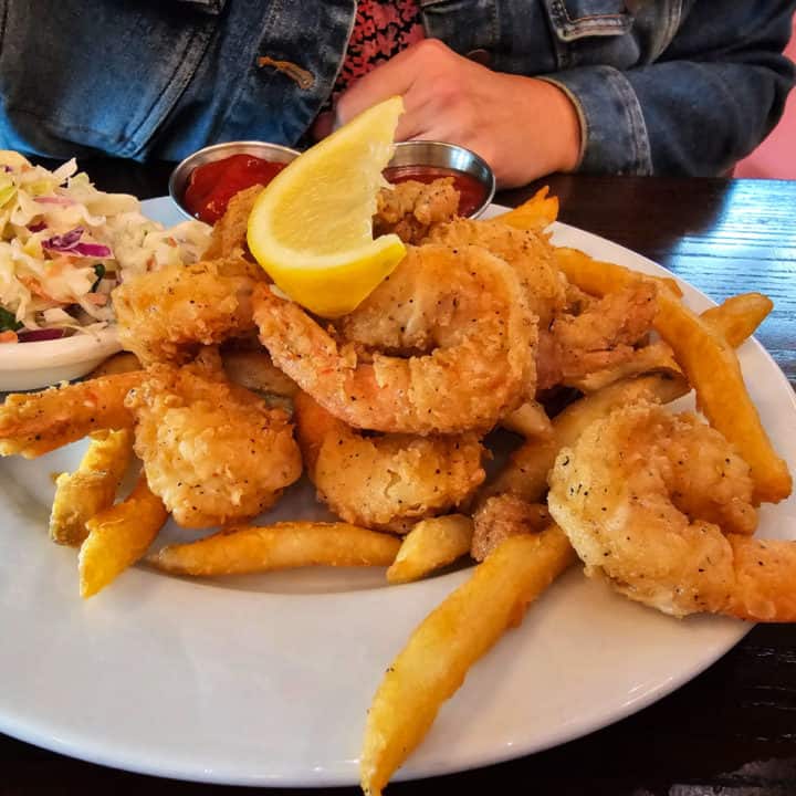 Fried shrimp on a white plate with fries, cole slaw, and cocktail sauce
