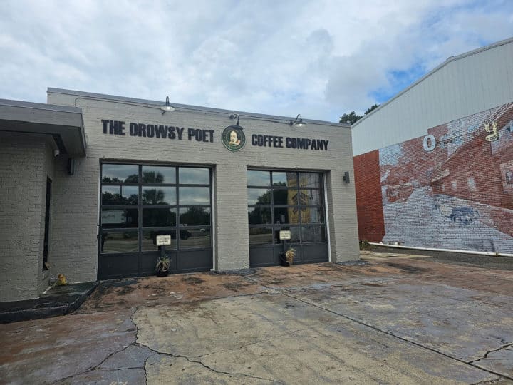 Exterior of brick building with The Drowsy Poet Coffee Company sign over two garage doors. Mural on the building to the right.
