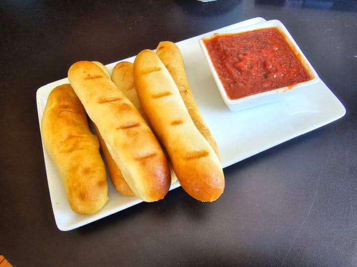 Garlic breadsticks on a white platter next to tomato sauce