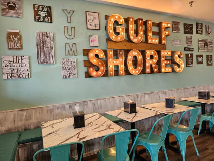 tables with benches and turquoise chairs below a light up Gulf Shores Sign in Island Ice Cream