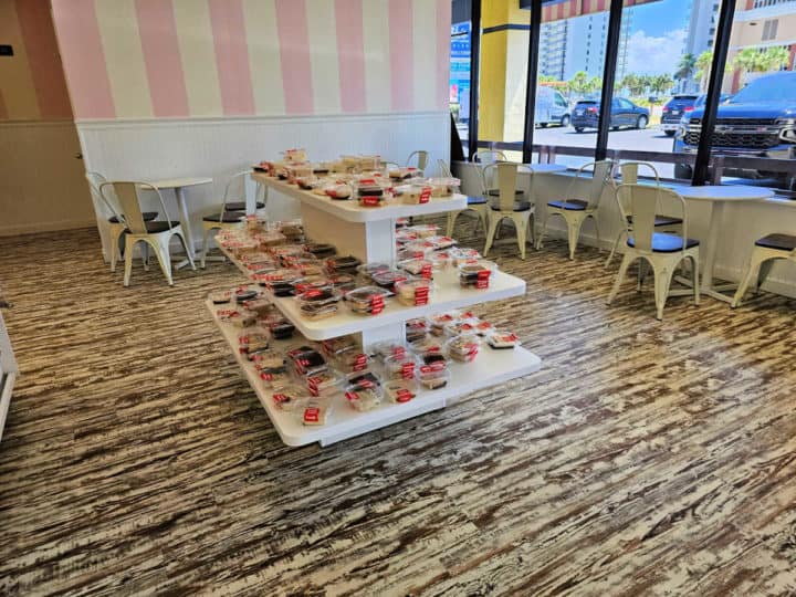 tables and chairs near a display of chocolate fudge and a pink and white striped wall