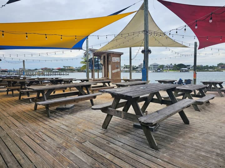 Outdoor seating with picnic tables on a deck and in the sand outside of the Flora Bama Yacht Club