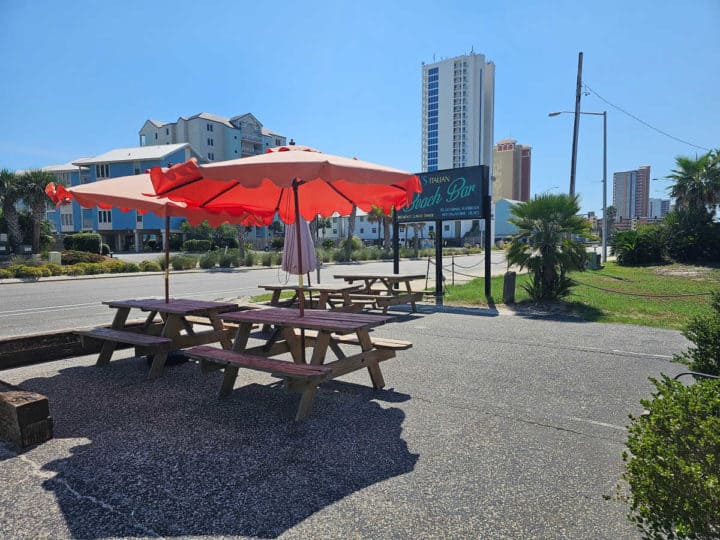 Picnic tables with red umbrellas by the Lauria's beach bar sign