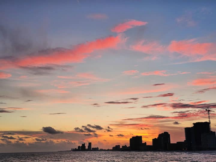 sunset with pink clouds over the water with gulf shores skyline in the background