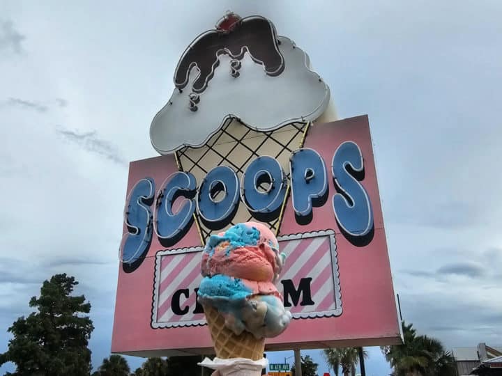 Rainbow ice cream cone in front of the Scoops Ice Cream sign