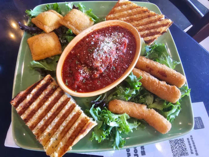 Appetizer sampler plate with fried ravioli, cheese sticks, garlic bread, and a bowl of marina sauce 