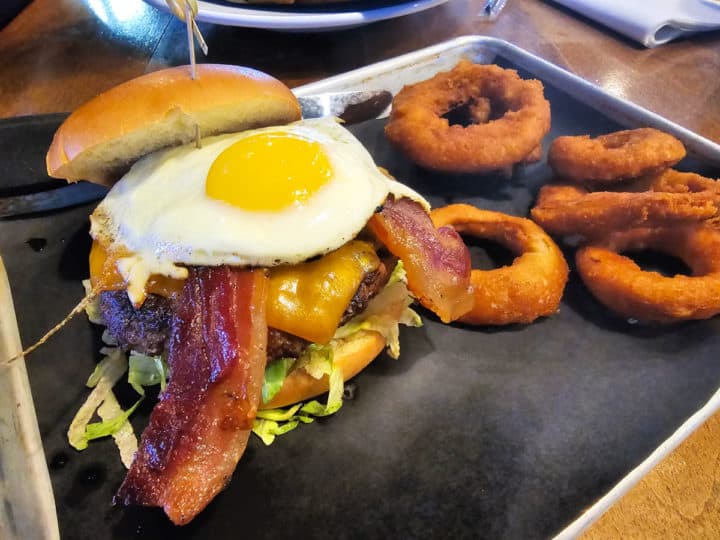 Bar burger with an egg on top next to onion rings on a silver tray