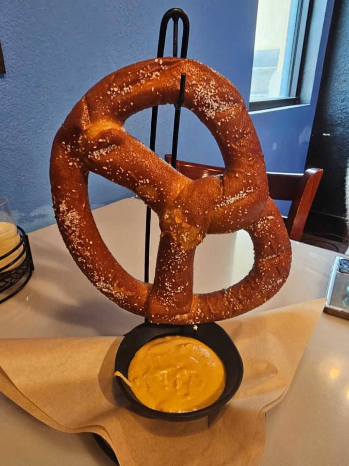 large Bavarian pretzel hanging over a bowl of cheese dip