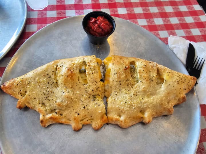 calzone on a pizza pan with a container of marinara sauce