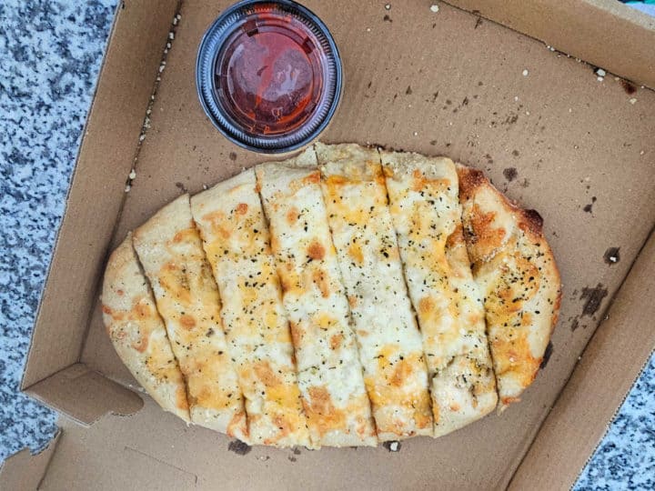 Cheesy bread in a delivery box with a container of marinara sauce