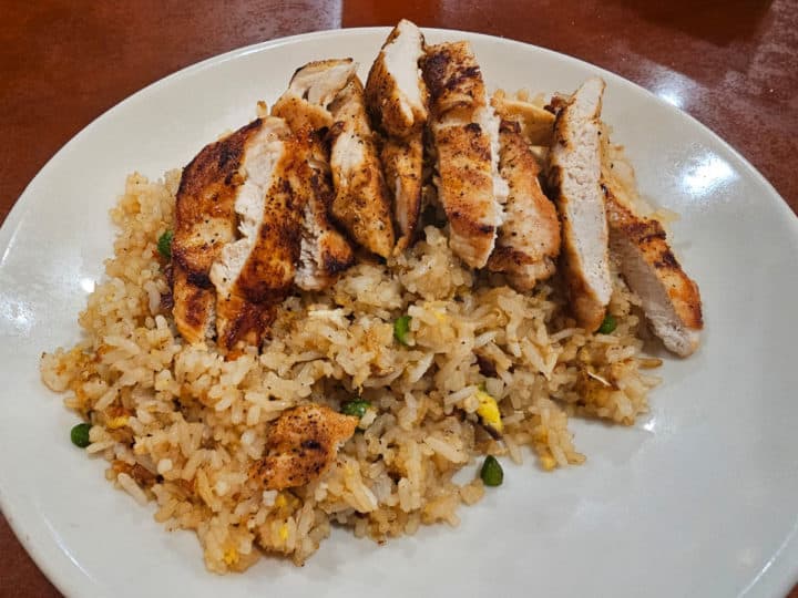 grilled chicken on fried rice on a white plate