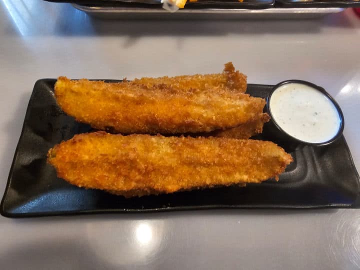 fried pickle spears next to a container of ranch on a black plate