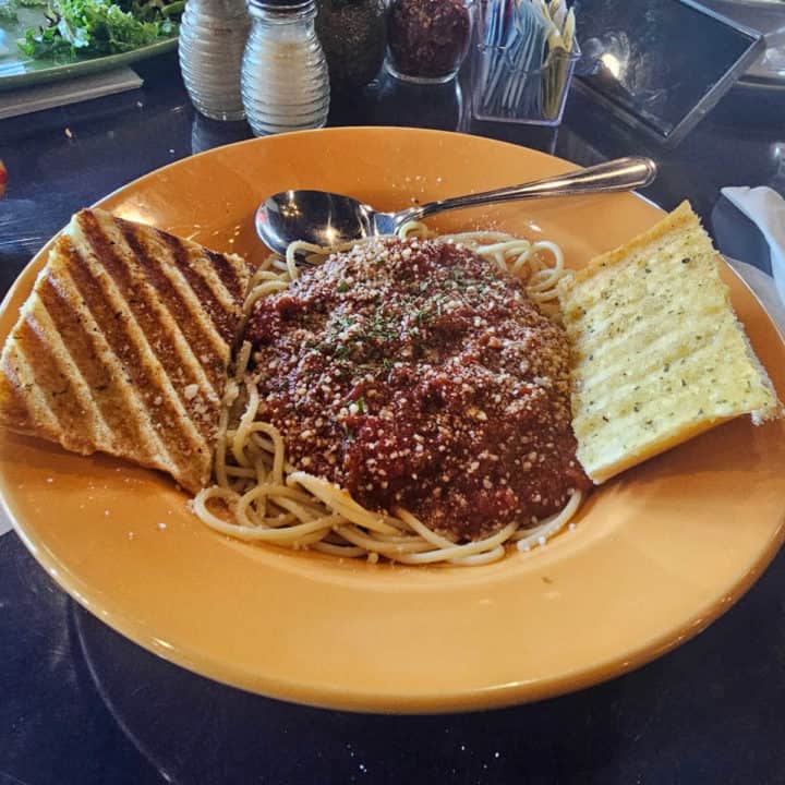 spaghetti and meat sauce on a yellow plate with garlic bread