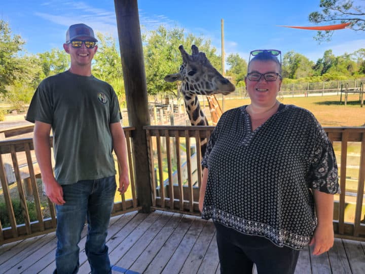 Two people standing with a giraffe in the middle of them. 