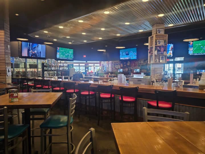 Indoor bar with stools around it and TVs on the wall