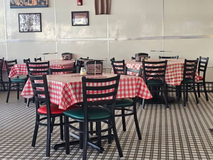 indoor seating with tables covered in red checkered table clothes, dark chairs, and a checkered floor. 