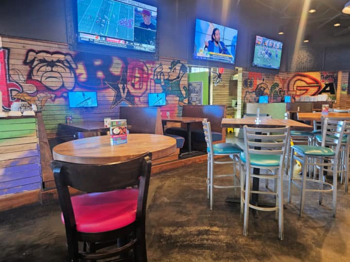 indoor tables and chairs with TVs on the wall along with college team mascots