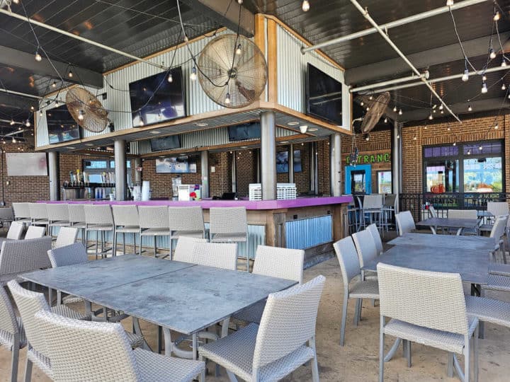 outdoor tables and chairs next to a bar with multiple TVs