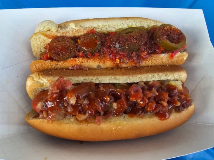 two hot dogs covered in jalapenos and relish in a paper container. 