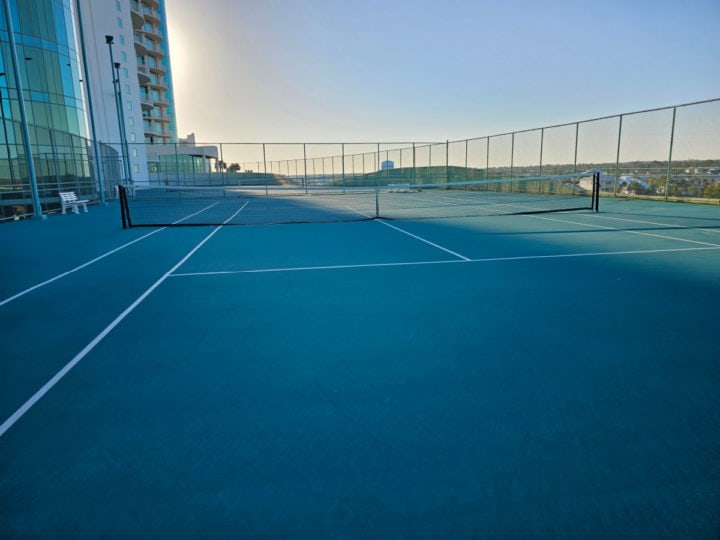 tennis courts with a building next to them and large fence 