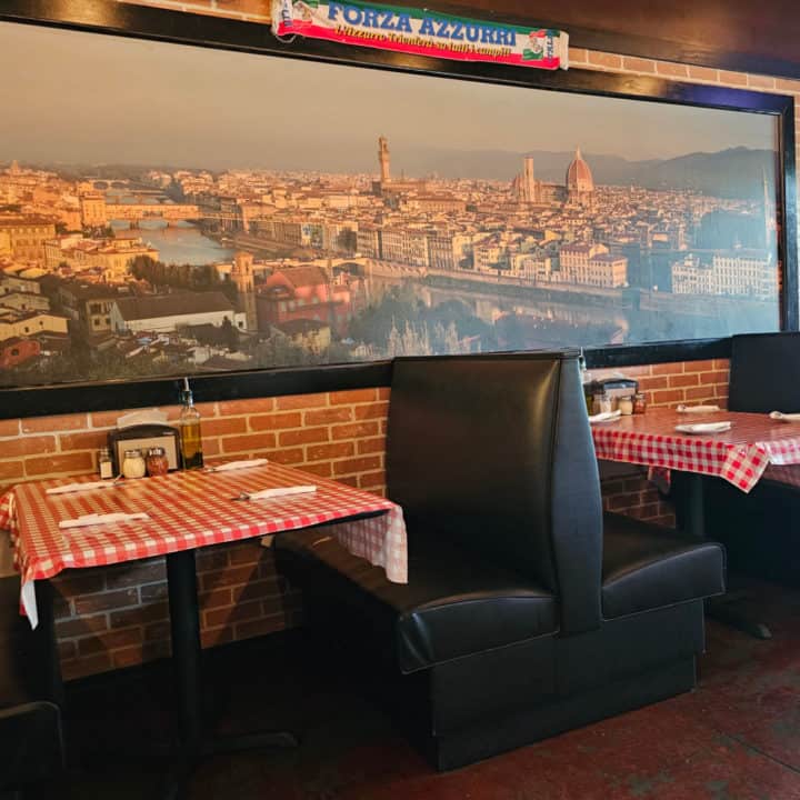 red checkered table cloth next to leather booths below a photos of Italy