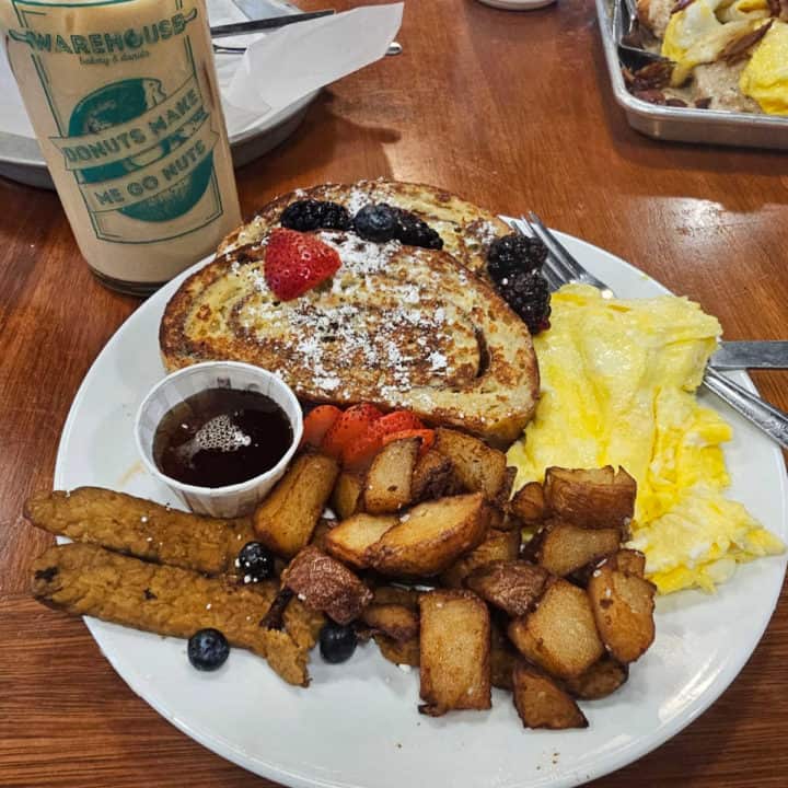 Warehouse Bakery and Donuts glass next to a plate with cinnamon roll french toast, veggie bacon, potatoes, and scrambled eggs