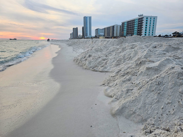 Sand built up along the shore line with sunset and buildings in the background