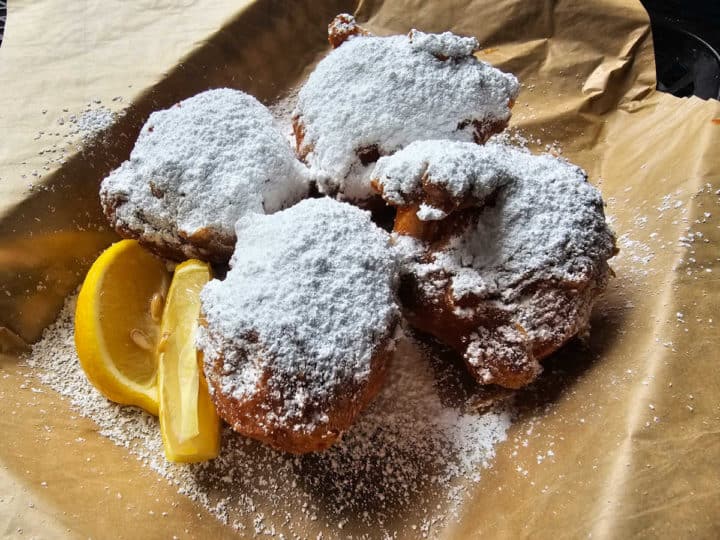 Powdered sugar covered beignets on parchment paper next to lemon slices