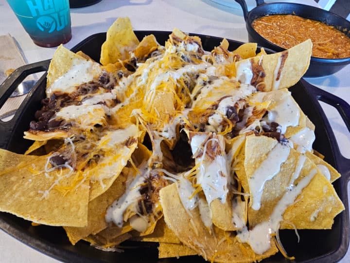 Nachos covered in cheese with a bowl of chicken in the background