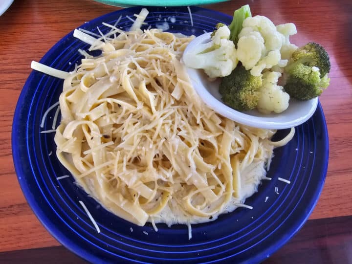 Fettuccine alfredo on a blue plate with a side of steamed broccoli and cauliflower