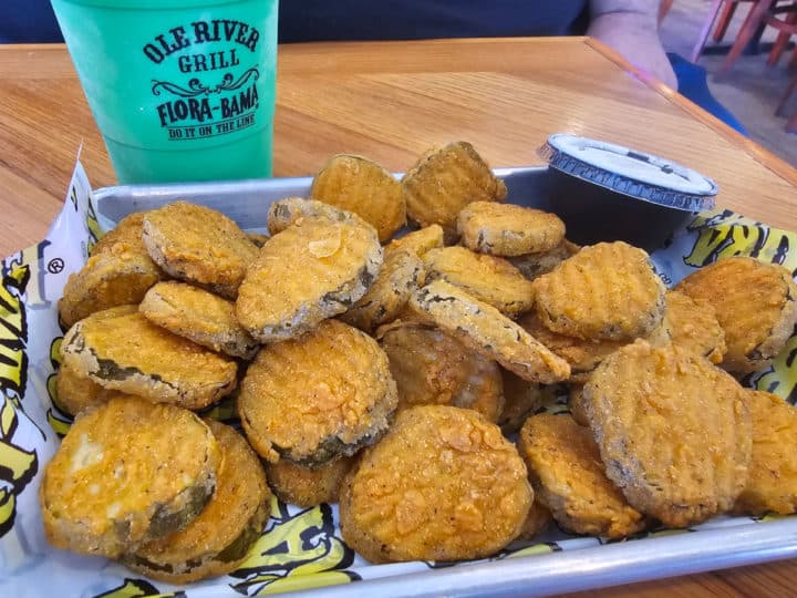 Fried pickles on a metal tray with ranch next to a Flora Bama Ole River Grill cocktail cup
