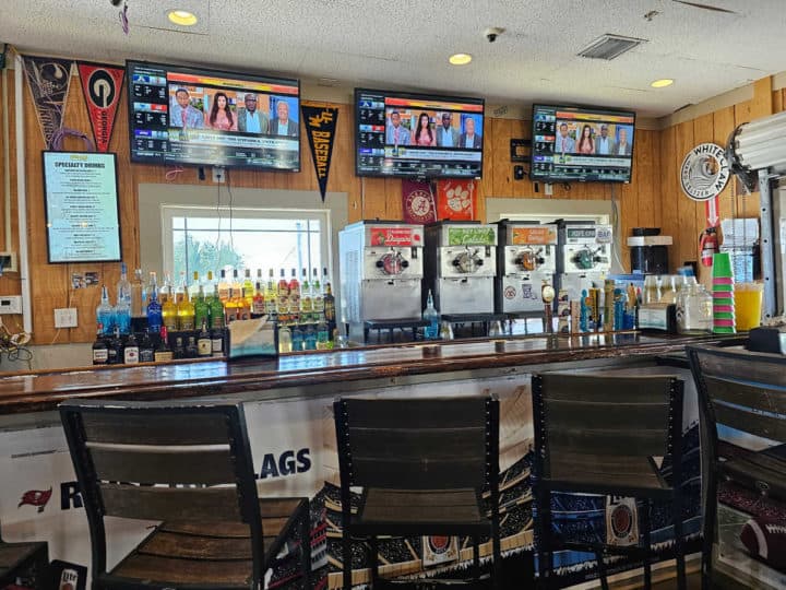 Bar stools up against a bar with drink machines and tv's