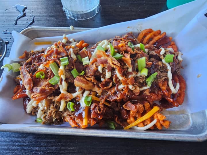 sweet potato fries covered in pulled pork, bacon, cheese, and green onions