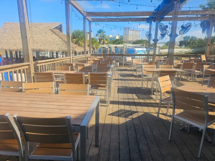 outdoor tables and chairs on a deck with fans above them