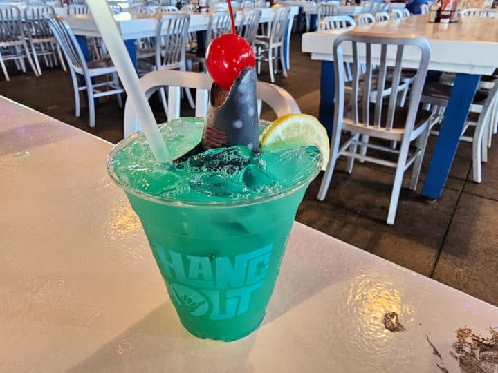 Shark attack drink with a shark holding a cherry in a green blue drink