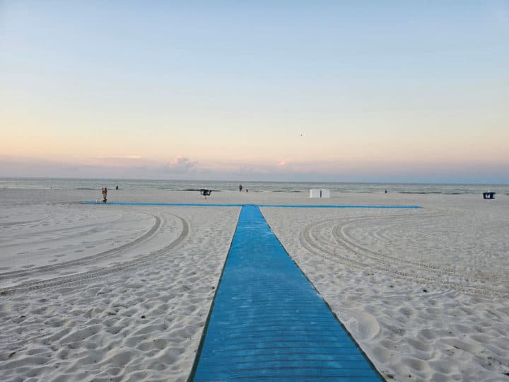 Blue wheelchair accessibility mat on white sand with the sunrise in the background. 