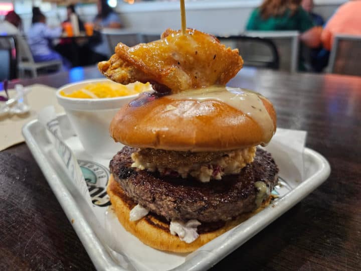 Burger in a silver tray with a chicken wing on top of the burger