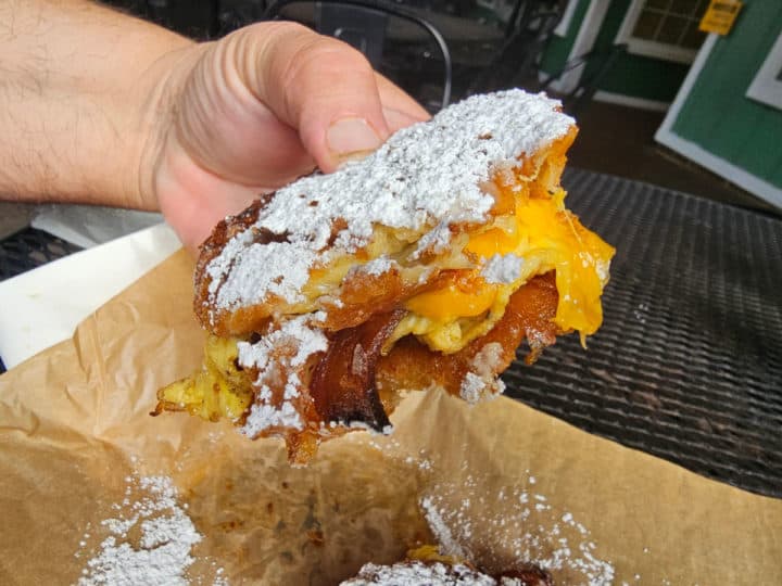 Hand holding a beignet slider with melted cheese and bacon