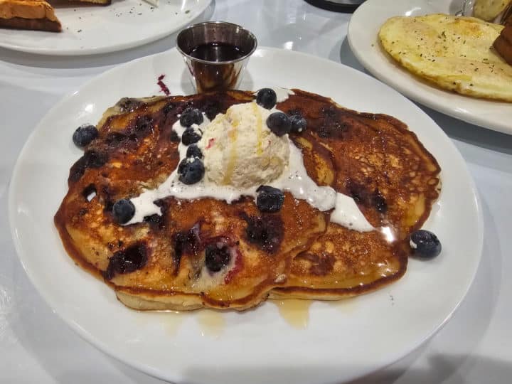 Blueberry Ricotta pancakes on a white plate next to a container of syrup