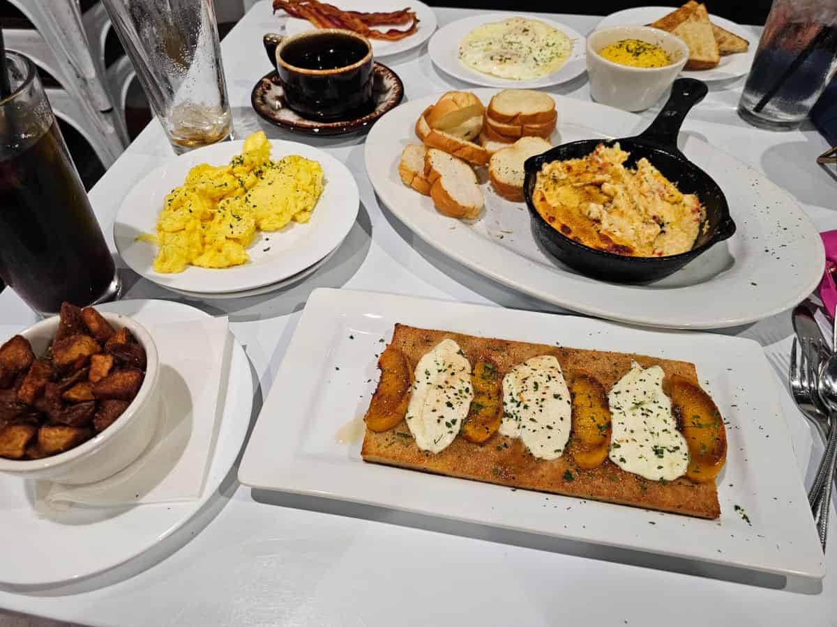 plates spread across the table with breakfast potatoes, eggs, burrata peach flatbread, pimento cheese dip, toast, and bacon