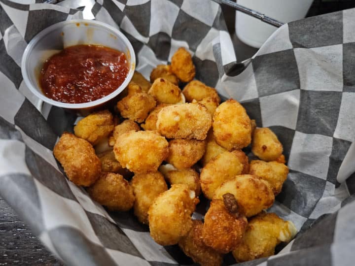cheese curds in a checkered paper lined basket with a cup of marinara sauce