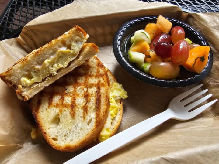 egg and cheese breakfast sandwich next to a bowl of fruit in a parchment lined basket