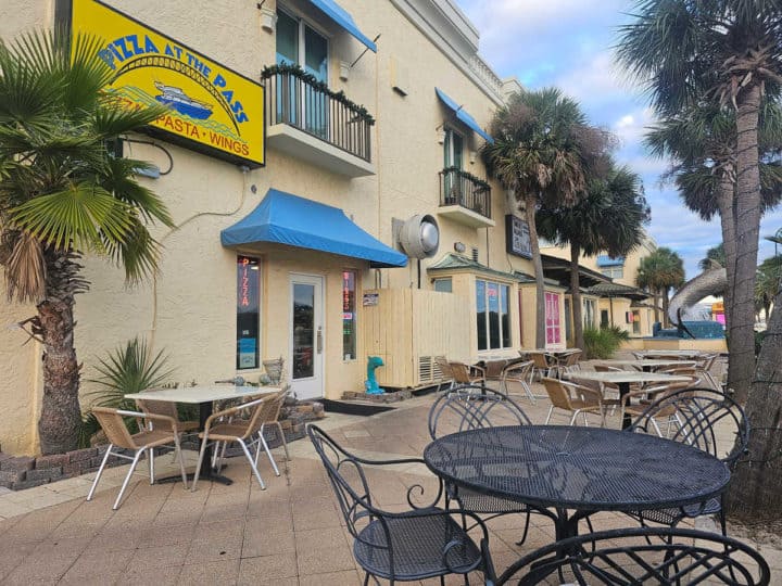 Pizza at the Pass sign over a blue awning and front entrance with tables and chairs on the patio