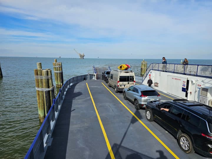 cars lined up in the middle of a ferry at the dock with people standing on a platform. 