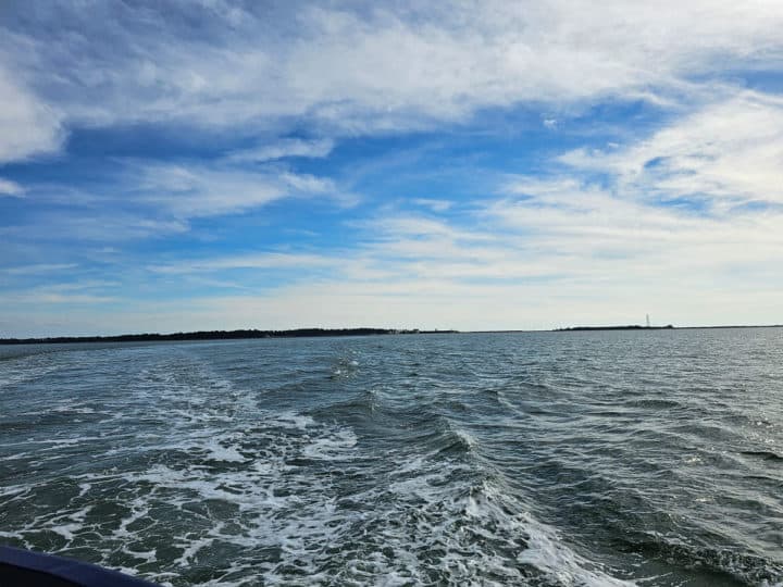 ferry wake in the water with blue skies and bright white clouds