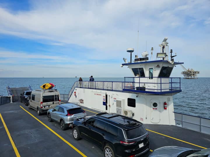 Looking over a ferry with cars lined up and a platform with passengers 